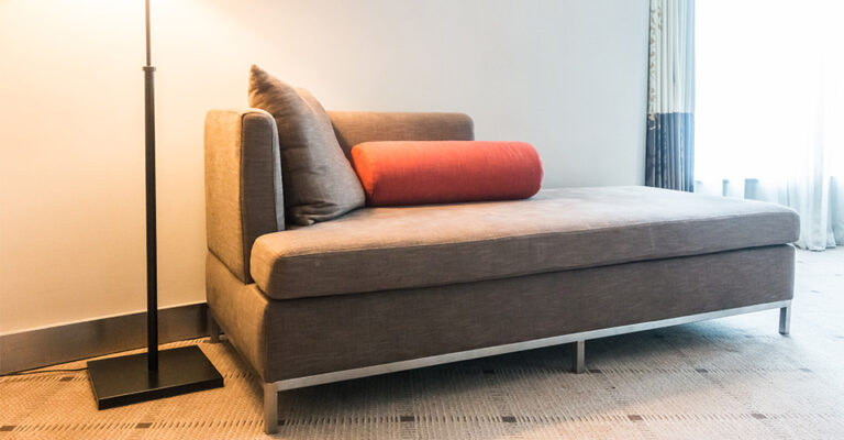 Canapé convertible gris avec coussin rouge et lampe sur pied dans un salon contemporain lumineux